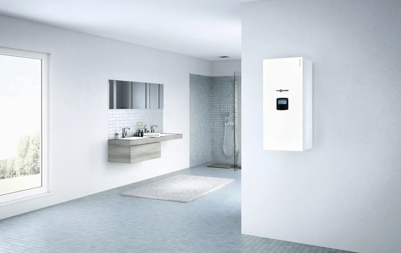Weißer elektrischer Heizkessel von Viessmann an einer hellen Wand in einem modernen Badezimmer, mit Dusche und Waschtisch im Hintergrund.